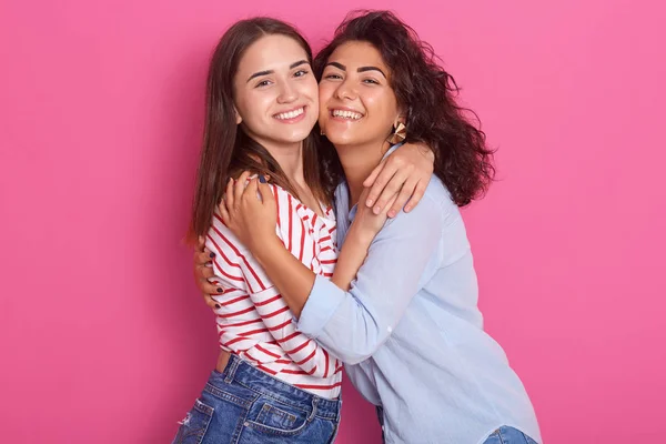 Innenaufnahme von zwei schönen Mädchen. Eine junge Frau umarmt eine andere, Damen blicken lächelnd direkt in die Kamera, tragen lässige Hemden, brünette lesbische Frauen isoliert über rosa. Ein Sex-Liebe-Konzept. — Stockfoto
