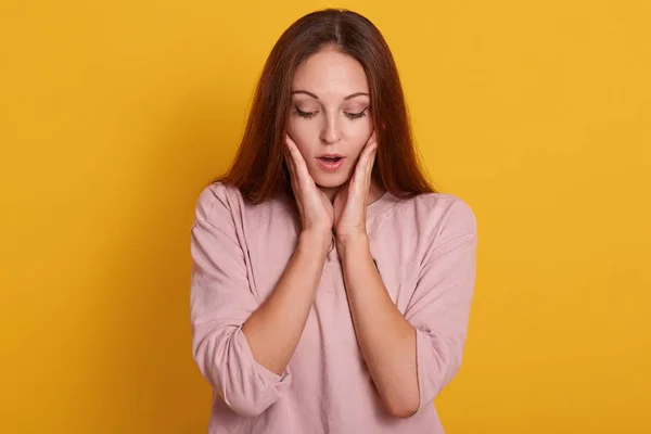 Retrato de cerca de la hermosa chica sorprendida sosteniendo sus manos cerca de las mejillas y mantiene la boca abierta, la atractiva dama está en asombro, posando aislada sobre el fondo amarillo. Gente emociones concepto . — Foto de Stock