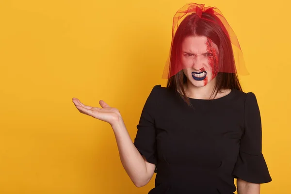 Retrato de cerca de una hermosa joven con una herida sangrienta en la cara, modelo posando aislada sobre un fondo amarillo, extendiendo su brazo a un lado, con expresión facial enojada. Concepto Halloween . — Foto de Stock