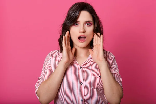 Primer plano retrato de chica sorprendida con la boca abierta, se mantiene cerca de la cara, modelando aislado sobre fondo de estudio rosa, usando blusa, tener el pelo oscuro, se ve asustado. Gente emociones concepto . — Foto de Stock