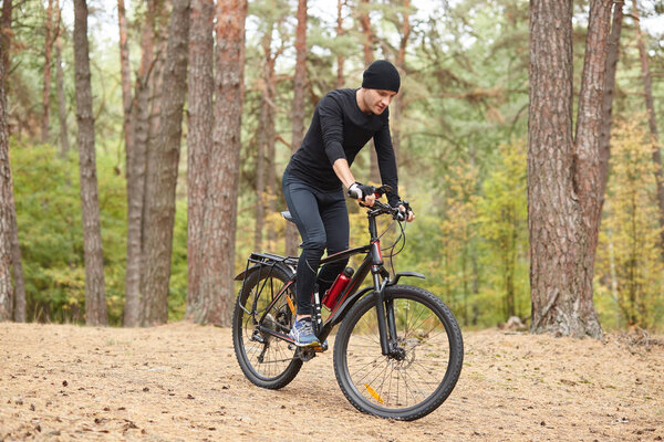 Photo of cyclist on forest trail, trip on bikes in lush green nature, young attractive guy wearing black sportwear rides around trees in forest, spends free time in open air. Healthy lifestyle concept