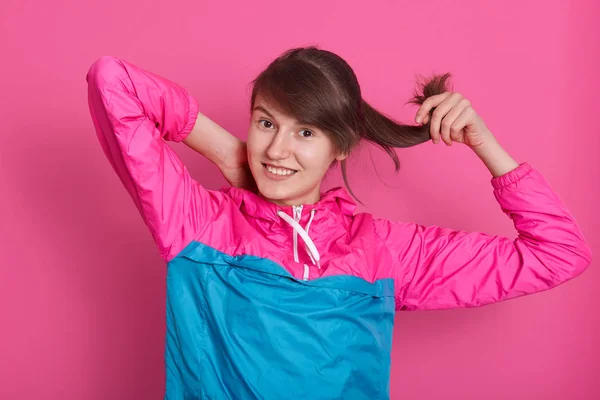 Beeld van een fitnessvrouw die in de studio over een roze achtergrond staat, direct lachend naar de camera kijkt, stijlvol blauw roossportschoeisel draagt, donker steil haar heeft. Gezond levensstijl concept — Stockfoto
