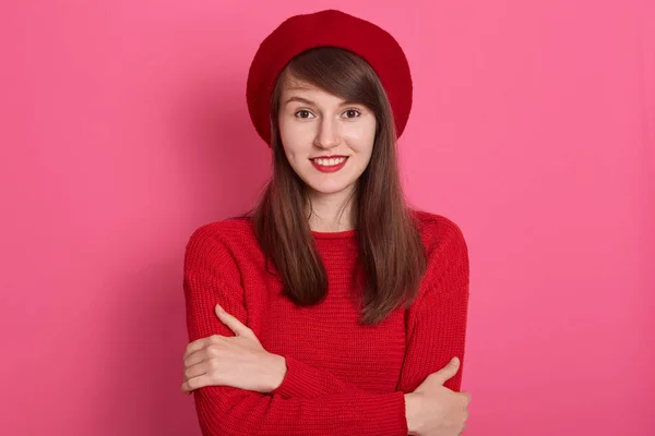 Close up retrato de atraente elegante jovem mulher vestindo boina vermelha brilhante e camisa de pé contra a parede rosada, olhando diretamente para a câmera com sorriso, encantadora fêmea com aparência agradável . — Fotografia de Stock