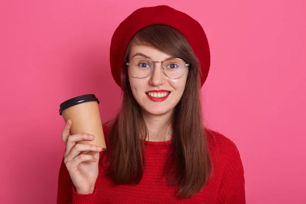 Горизонтальный снимок веселой женщины, одетой в свитер и красный берет, округлые очки, держащей кофе или чай в бумажной одноразовой кепке, смотрящей в камеру с изумленным выражением лица, эмоциями людей . — стоковое фото