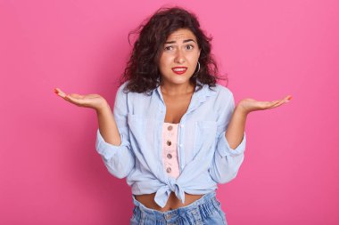 Yanlış anlaşılmış bir kadının omuz silkip doğrudan kameraya baktığı bir fotoğraf. Güzel bir kadın ellerini açıyor, kot pantolon ve mavi gömlek giyiyor, pembe arka planda soyutlanmış poz veriyor..