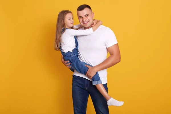 Indoor shot of loving daddy holding at little adorable daughter feeling love isolated over yellow studio background. Deep devotion and warm relationships, closest person, fathers day concept. — Stock Photo, Image