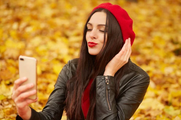 Technológia internet és boldogság koncepció. Nő csinál szelfi a parkban, boldognak tűnik, hogy önkép okostelefon kamera szabadban, modell pózol őszi parkban, körülvéve arany levelek. — Stock Fotó