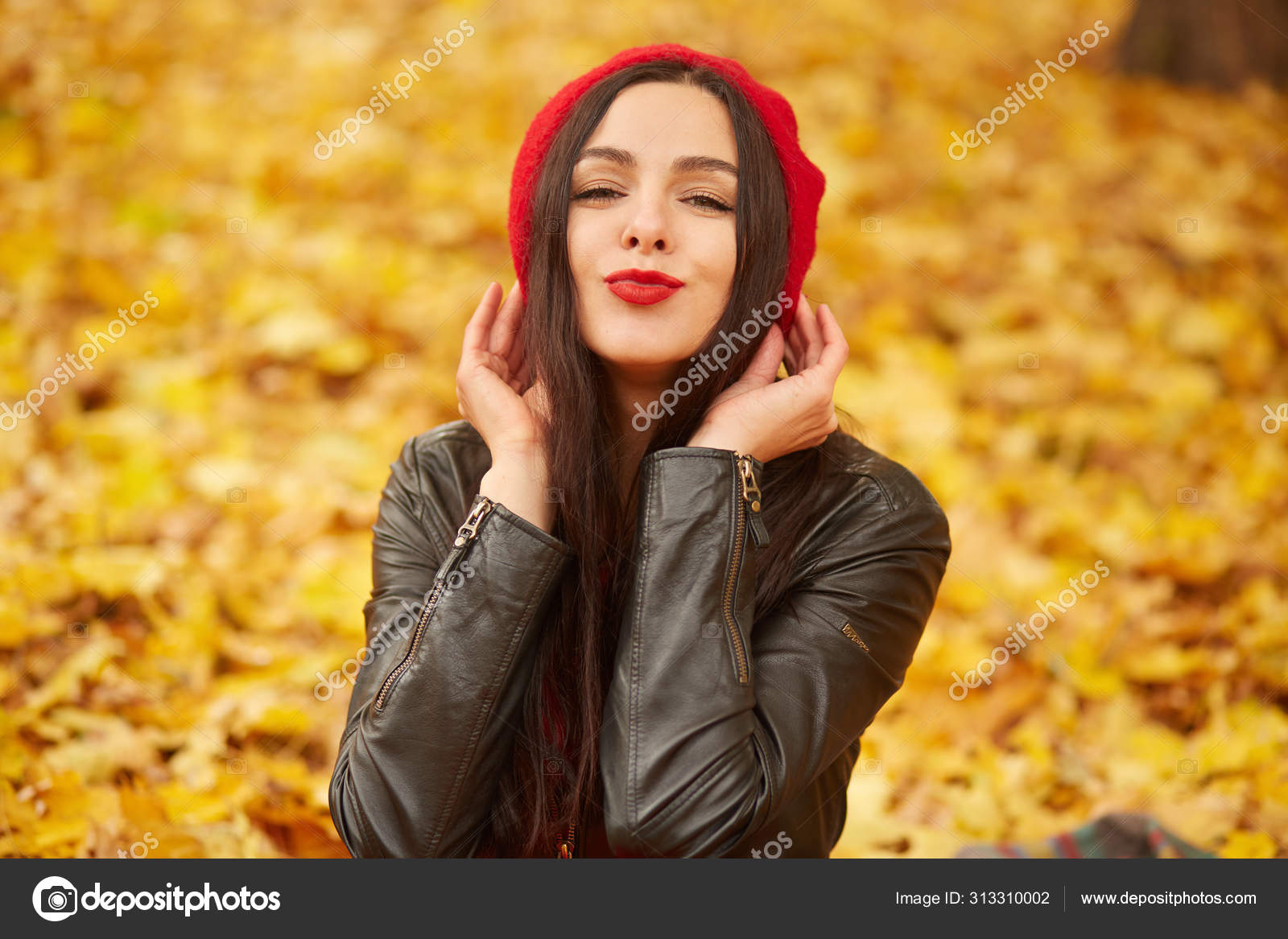 Horizontal shot of beautiful woman showing kiss gesture and smiling to  camera, posing outdoor on autumn park background, charming girl dresses red  beret and leather jacket, surrounded yellow leaves. Stock Photo by ©
