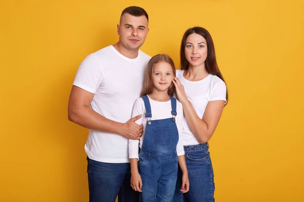 Image of happy Caucasian family pose smiling isolated over yellow background, parents with cute little daughter enjoy spending together, dress casual outfits, looking at camera. Happyness concept. — Stock Photo, Image