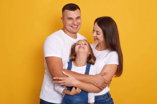 工作室里年轻快乐的高加索家庭形象。 父亲，母亲和他们的小女儿，家人拥抱在一起，在黄色的工作室背景上摆出孤立的姿势。 爱与幸福的概念. — 图库照片