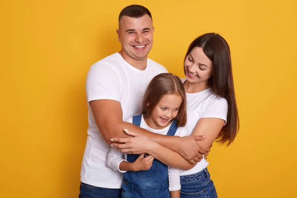 Close up portrait of young Caucasian family.Father, mother and charming daughter. Parents hugging little cute child dressed denim overalls. Woman and man smiling, expressing love and happyness. — Stock Photo, Image