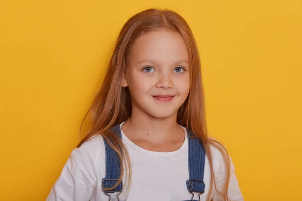 Beltéri felvétel gyönyörű kislány hosszú szőke haj pózol elszigetelt sárga háttér, nézi a kamera, bájos gyerek visel alkalmi ruhát, hogy boldog, hogy fotózták a stúdióban. — Stock Fotó