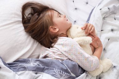 Tatlı küçük kız yatakta uzanıyor, bütün gün oynadıktan sonra uykuya dalıyor, battaniyenin altında gözleri kapalı beyaz yastığa uzanıyor, çekici çocuk pijama giyiyor, kadın çocuk odasında dinleniyor. Çocukluk kavramı