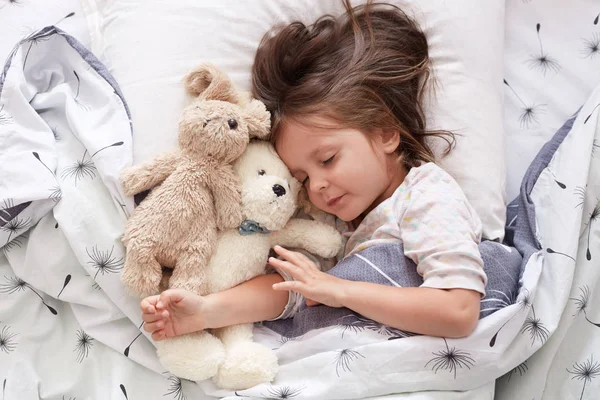 Douce petite fille dormant avec des jouets dans la crèche. Gros plan portrait d'un nourrisson dormant dans un lit bébé. Beau tout-petit dormant avec ours jouet et chien, bébé fatigué se détendre. Doux coucher et concept d'enfance .. — Photo