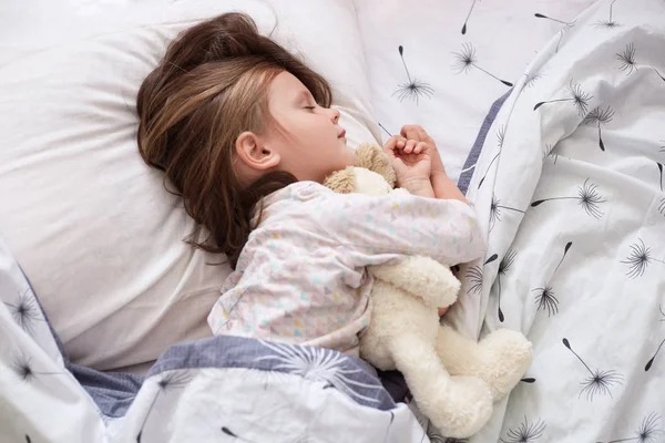 Aranyos kis lány mackó ágyban alszik — Stock Fotó