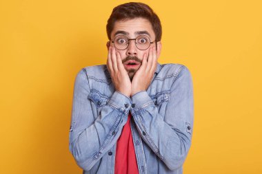 Duygusal olarak şok olmuş, gözünü ve ağzını açan, ellerini yüzüne koyan, yüz ifadesini etkileyen kot ceket ve kırmızı tişört giyen adamın portresi. İnsanlar ve duygular.