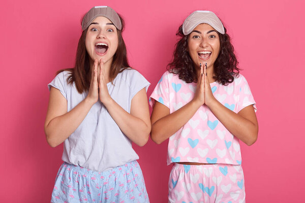 Horizontal shot of emotional joyful cute funny brunettes looking directly at camera, putting hands together, doing exercises in morning after sleep, wearing pajamas, being active. Youth concept.