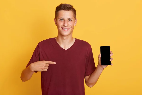 Sonriente Chico Alegre Sosteniendo Teléfono Con Pantalla Blanco Señalándolo Con — Foto de Stock