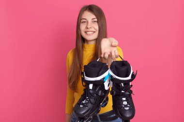 Beyaz tenli, elinde patenle gezen, spor malzemelerini gösteren, doğrudan kameraya bakan, aktif bir şekilde zaman geçiren, olumlu duygular ifade eden bir kadın..