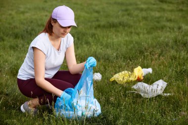 Çayırdan plastik şişe ve çöp toplayan bir kadın, plastik çöp toplayan bir çevreci, yeşil alandan tek kullanımlık plastik toplamaya gönüllü..