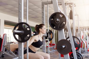 Sağlık kulübünde ağırlık kaldırarak halter kullanan genç bir kadın. Spor giyimli kadın ve atkuyruğu spor salonunda çömelirken, fitness modeli kilo alır ve güç kazanır..