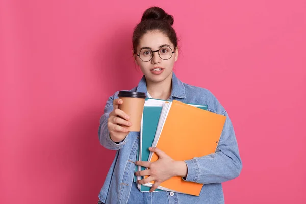 黑头发的女学生提供外卖咖啡 手里拿着纸夹 站在粉红色的背景上 女士在课间休息时喝咖啡 — 图库照片