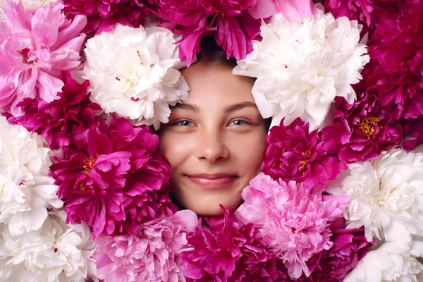 Smiling woman surrounded with white, pink and burgundy peonies, female with pleasant appearance and good mood, looking directly at camera, charming lady with flowers.