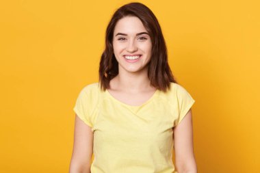 Sarı arka planda gülen genç bir kadın, dişlek bir gülümsemeyle poz veren esmer bir bayan, iyi haberler, iyi bir ruh hali içinde olmak, mutluluğu ifade etmek..
