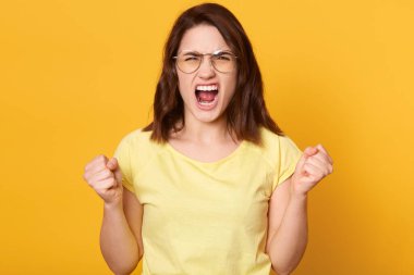 Kızgın, gözlüklü, vahşi bir ifadeyle bağıran, çok üzgün, koyu saçlı, deli gibi bağıran, sarı tişörtlü, esmer bir kadın..