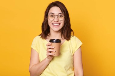 Gitmek için kahve içen güzel genç bir kadın, heyecanlı bir yüz ifadesiyle poz veren, günlük kıyafetler ve gözlük takan bir kadın, gülümsüyor, çok mutlu görünüyor..