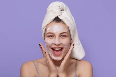 Su jölesi maskesi takan, cilt bakımı için yüz maskesi kullanan mutlu ve heyecanlı görünen, avuç içlerini yanaklarında tutan, mutlu bir şekilde bağıran, spa ameliyatlarından zevk alan bir kız..