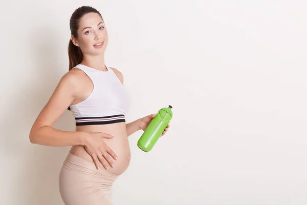 Mujer Embarazada Joven Sosteniendo Botella Agua Tocando Vientre Mirando Cámara — Foto de Stock