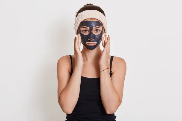 Jonge Ongelukkige Huisvrouw Met Zwart Cosmetisch Masker Gezicht Staan Geïsoleerd — Stockfoto