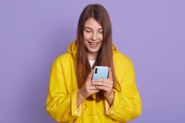 Mor arka planda tek başına duran güzel bir kadın, telefon ekranına bakıyor, arkadaşıyla veya kocasıyla sohbet ederken gülümsüyor, mutluluğunu ifade ediyor..