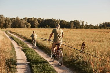 Baba ve oğul birlikte bisiklet sürerek arazide geziyorlar, olta ile balık avlamak istiyorlar, güneşli bir günü aktif olarak dinlenerek geçirmek istiyorlar..