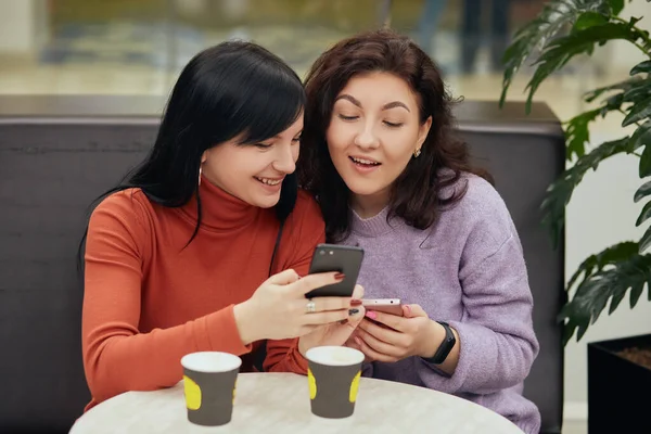 Two Excited Young Girls Using Mobile Phones While Sitting Table — Stock Photo, Image