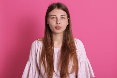 Güzel kahverengi kadın dudaklarının portresi erkek arkadaşından öpücük alacak gibi, kameraya flört ifadesiyle bakıyor, pembe arka planda izole edilmiş..