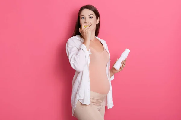 Atractiva Chica Embarazada Mordiendo Manzana Mientras Sostiene Botella Agua Mano — Foto de Stock