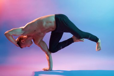Atletik kaslı genç adam yoga yapıyor vücut dengesi için egzersiz yapıyor, tek ayak üstünde duruyor, siyah pantolon giyiyor, güçlü adam duvarsız alanda antrenman yapıyor..
