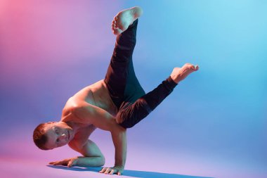 Güçlü, esnek bir adam sabah yoga egzersizleri yapıyor. Neon duvardan izole edilmiş, siyah pantolon giyiyor. Ciddi ve konsantre görünüyor..