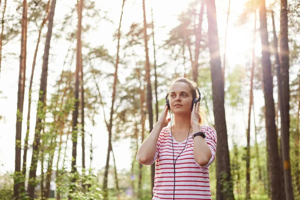 Çizgili Tişört Giyen Ormanda Müzik Dinleyen Etrafı Ağaçlarla Çevrili Kulaklıklarına — Stok fotoğraf