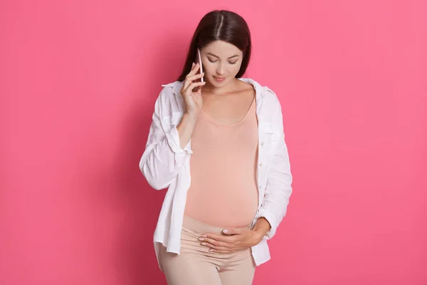 Беременная Женщина Изолированная Фоне Розовой Стены Разговаривает Мобильному Телефону Смотрит — стоковое фото