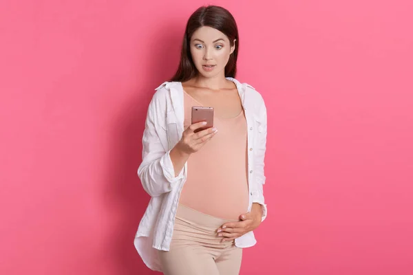Mujer Embarazada Asombrada Sosteniendo Teléfono Móvil Leyendo Algunas Noticias Impactantes — Foto de Stock