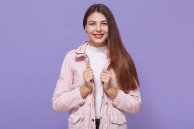 Çekici gülüşü olan gülümseyen bir kadın portresi, soluk pembe ceket giyen güzel bir kız, kameraya bakıyor, eflatun arka planda soyutlanmış poz veriyor..