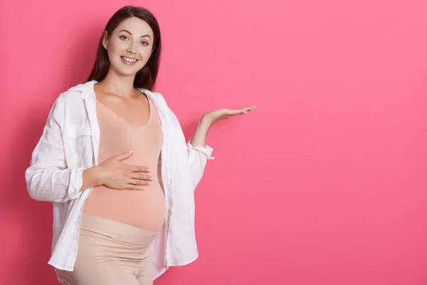 Feliz Mujer Embarazada Pie Sobre Fondo Rosa Extendiendo Palma Lado — Foto de Stock