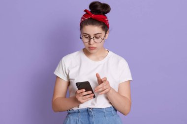 Az kambur saçlı bir kadın mutsuz yüz ifadesi olan bir cep telefonu kullanıyor, akıllı bir telefon tutuyor, sosyal ağda mesajlaşıyor, cep telefonunun ekranına bakıyor..