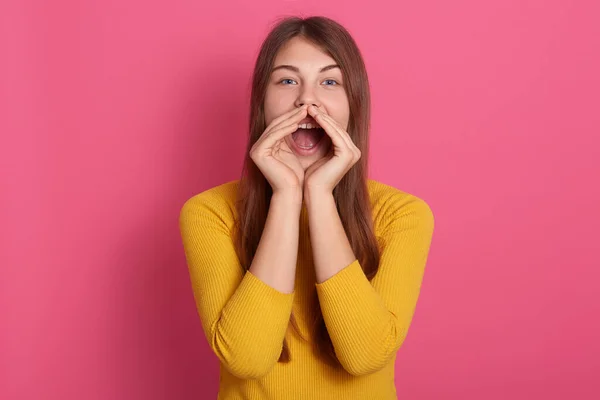 一个快乐有趣的年轻女人 穿着黄色毛衣 手牵着手尖叫着 嘴边隔着粉红的墙 一头长长的头发 大声尖叫着 — 图库照片