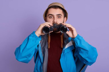 Yürüyüş yapan ve dürbünle bakan bir adam heyecan verici bir şey görüyor. Şok olmuş gözlerle bakıyor. Şapkalı, mavi ceketli ve kalın kazaklı..