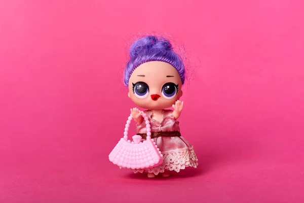 stuffed funny purple headed doll with beautiful big eyes, holds pink bag, wearing stylish rose dress, toy for girls isolated over pink background.