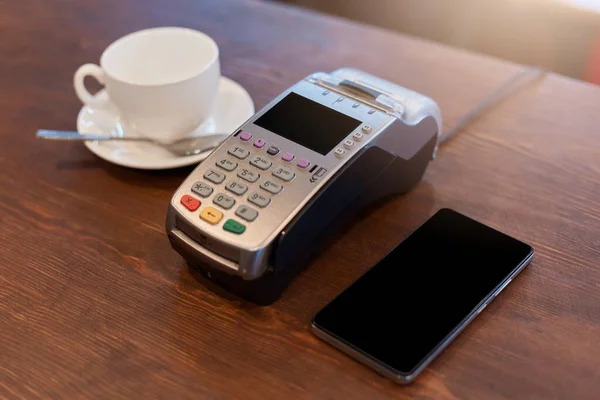 在咖啡店支付咖啡 白瓷杯 终端和带有空白屏幕的电话费用 购买无接触式支付装置 — 图库照片